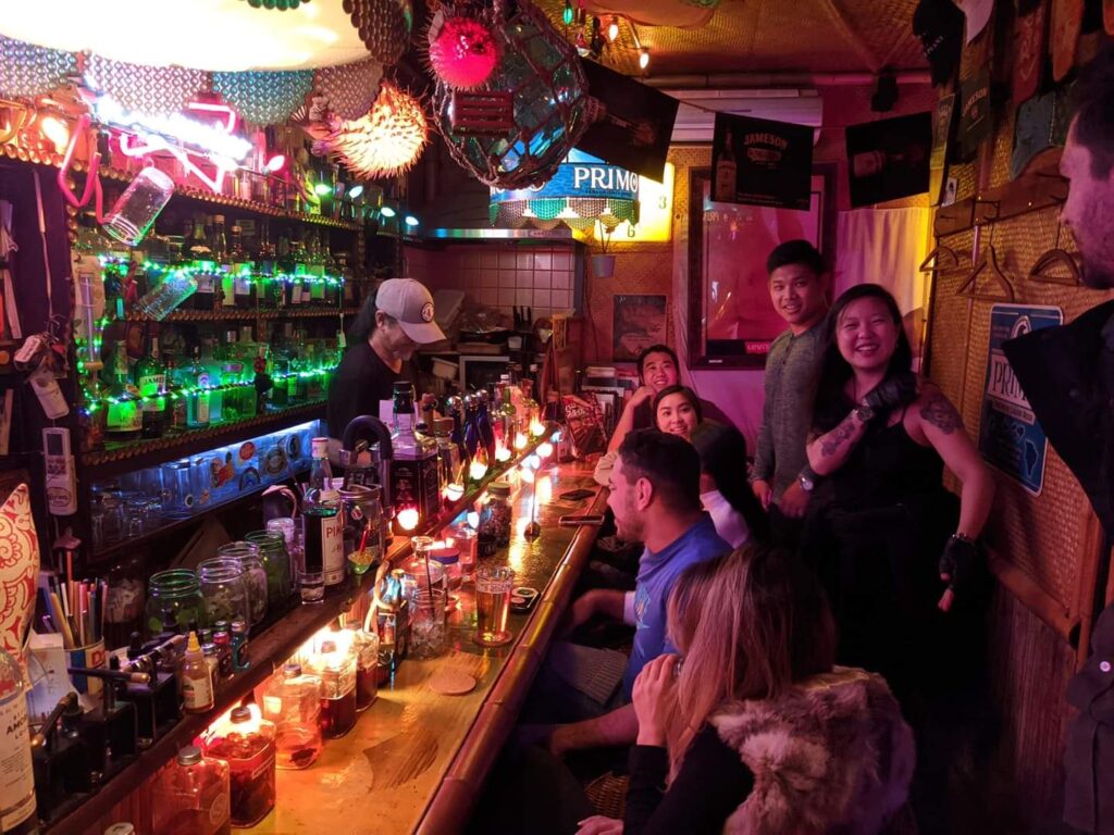 This is an image of a few people at a bar with many beers on tap and liquor bottles behind the bartender at a bar in Tokyo, Japan.