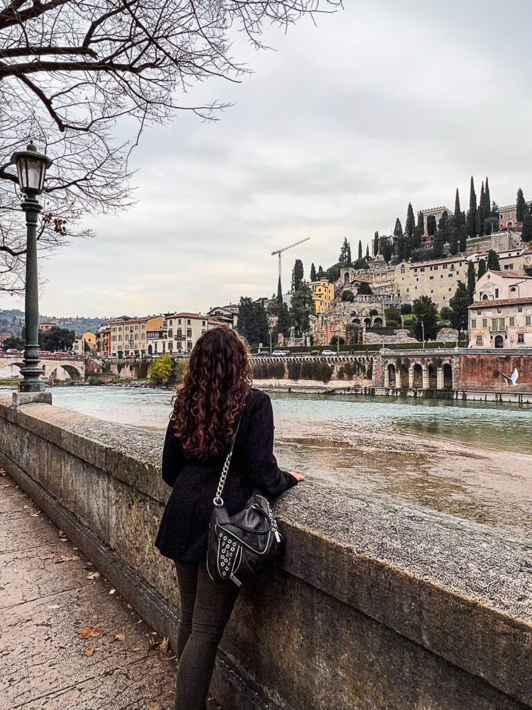 This is an image of the creator of The Purposely Lost with her back to the camera. She's looking out over the river in Verona Italy at the historic hill.