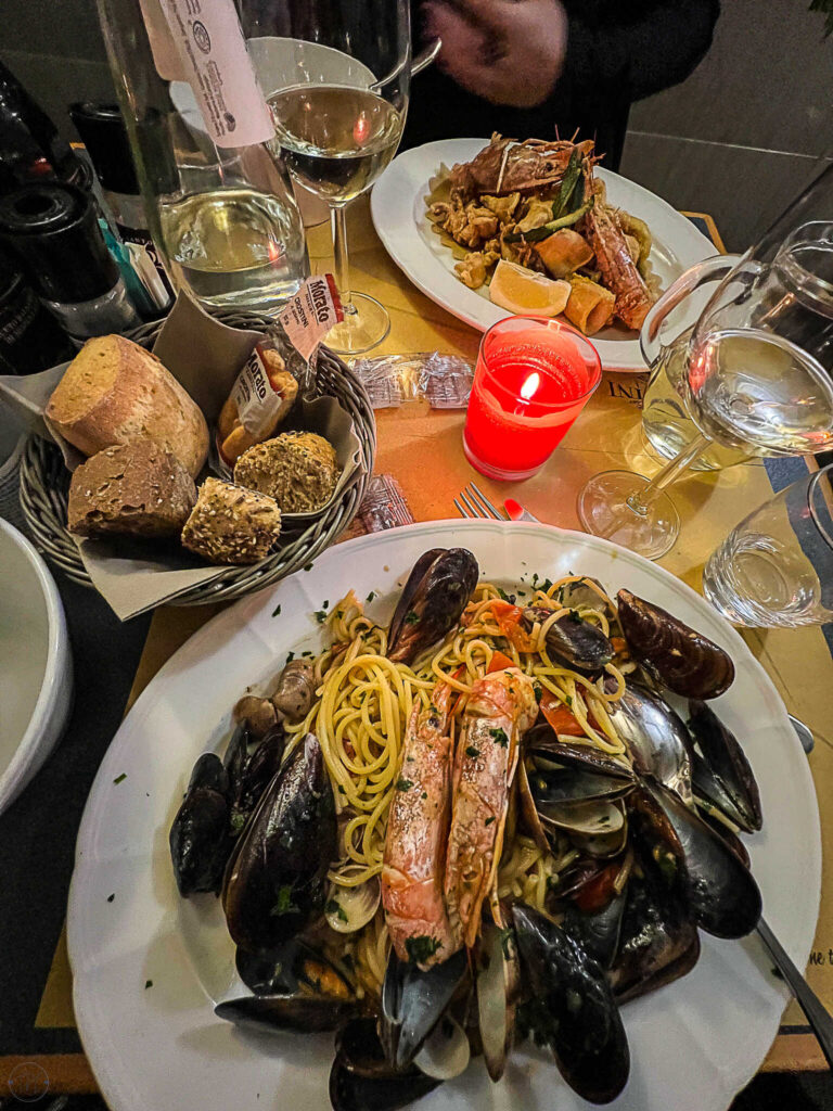 This is an image of a dinner in Venice Italy. The table has two plates of pasta. mussels, and bread on the candlelit table.