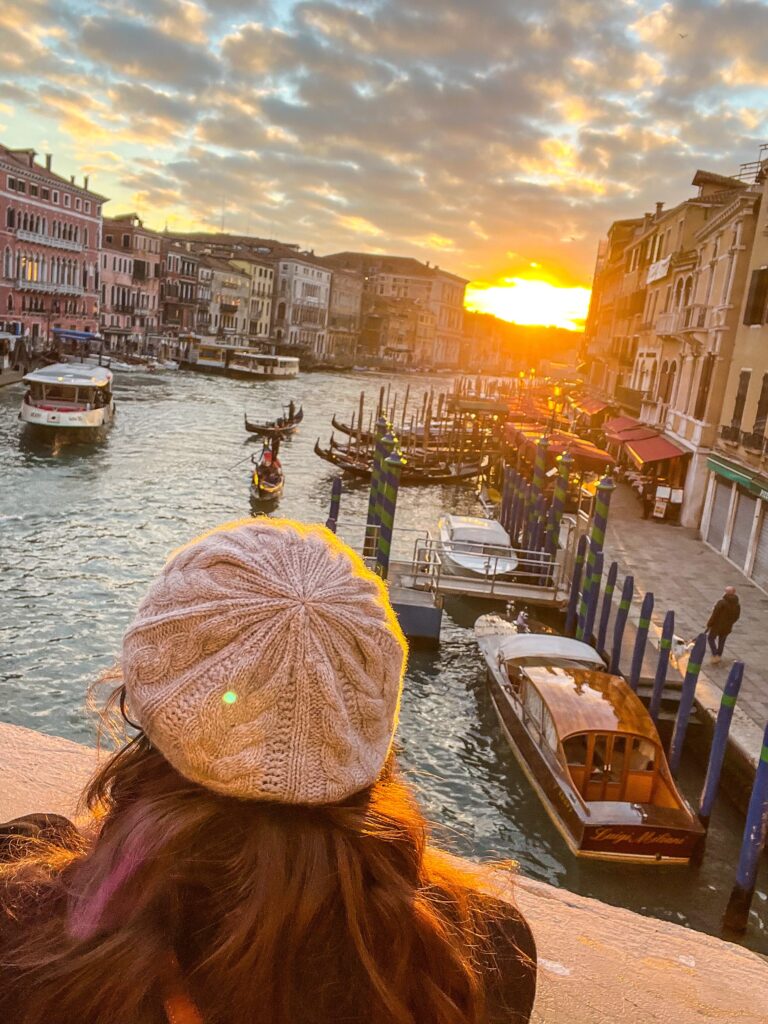 This is an image of the back of a woman's head looking out at the view on the Rialto Bridge at sunset in Venice Italy.