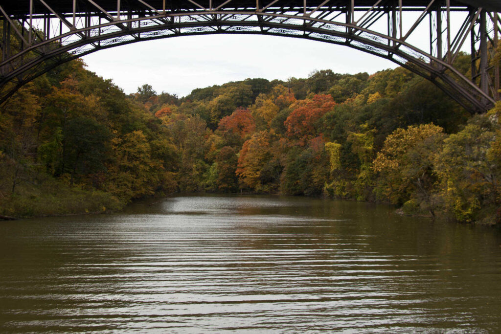 Bridge overarches autumn scene of river and colorful trees; New York State near Bear Mountain Bridge.