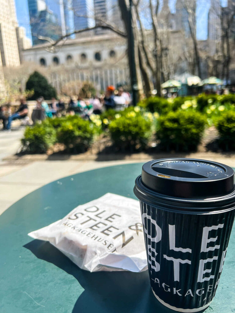 This is a coffee cup and cinnamon bun in Bryant Park in New York City.