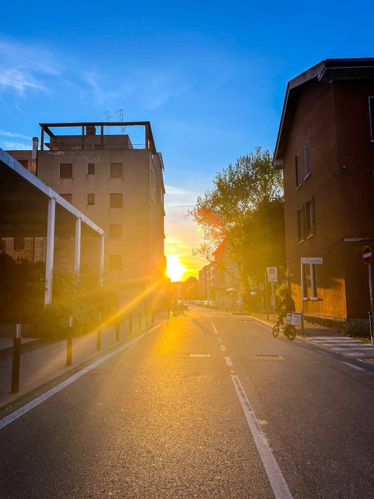 Sunset view down a quiet urban street with buildings on both sides, trees in the background, and golden sunlight reflecting on the pavement—unlike Venice, where many ask, "are there cars in Venice?.