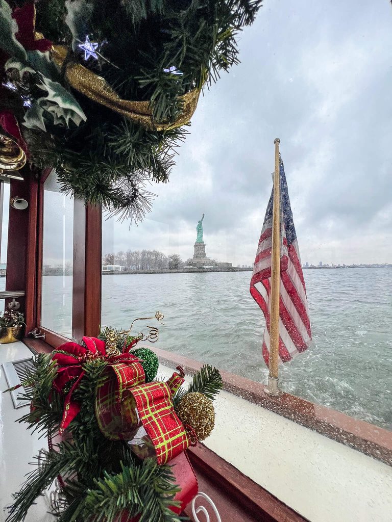 The Statue of Liberty viewed from a boat decorated with Christmas greenery and an American flag during a Christmas in New York tour.